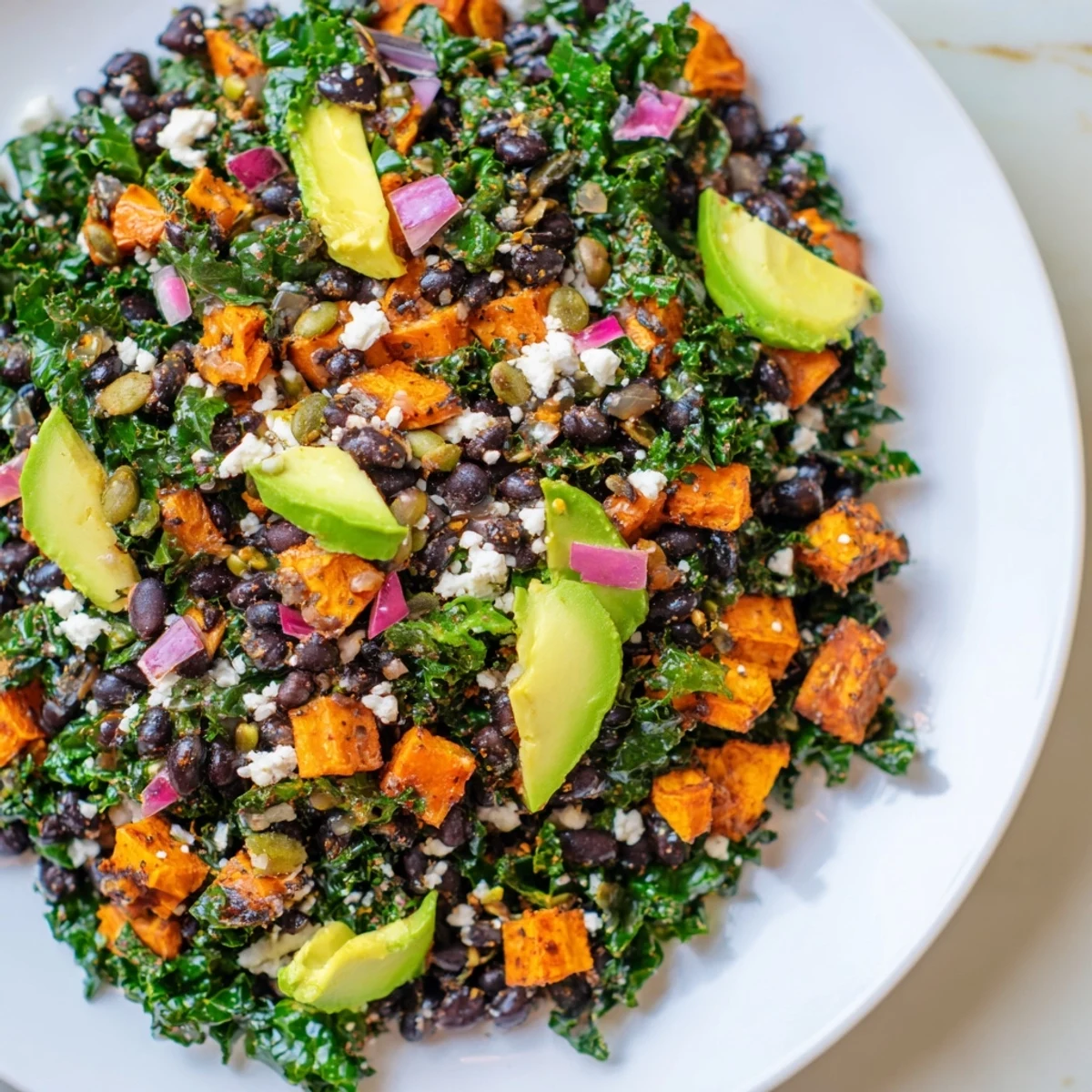 Vibrant massaged kale salad with roasted sweet potato, creamy avocado, and black beans drizzled in lime dressing.