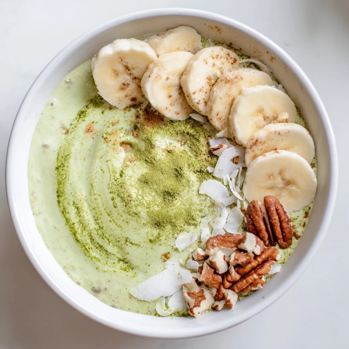 A bowl of vibrant green High-Protein Eggnog Matcha Overnight Oats, boasting hints of cinnamon and nutmeg.