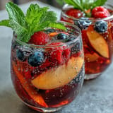 Vibrant Summer Sangria Mocktail with fresh peach and berries overflows a glass.