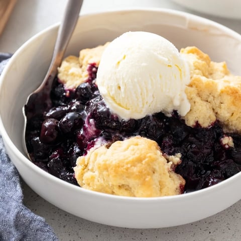 Warm blueberry cobbler topped with golden biscuits and served with vanilla ice cream.