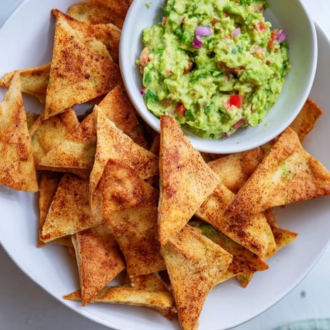 Golden, crispy pita chips surround a vibrant guacamole bowl, ready for dipping and enjoying.