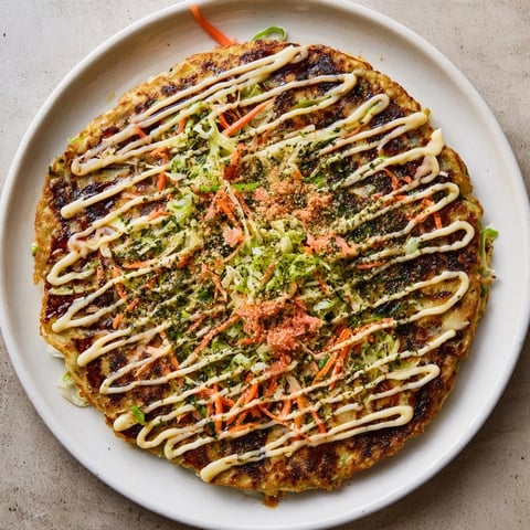 Golden-brown Japanese Okonomiyaki Pancakes sizzling on a griddle, topped with creamy mayonnaise, tangy sauce, and dancing bonito flakes.
