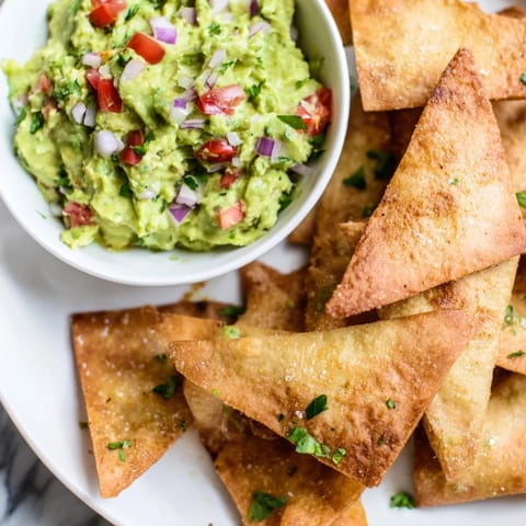 Fresh, creamy guacamole sits next to a pile of golden-brown pita chips, a perfect snack.