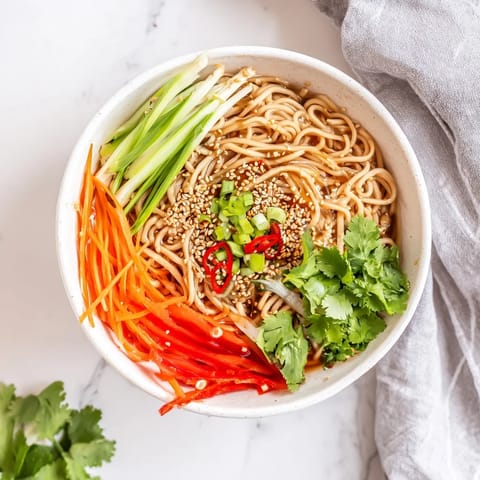 Close-up of a vibrant Asian Garlic Noodle Bowl, garnished with toasted sesame seeds and sliced red chili for a spicy kick.  