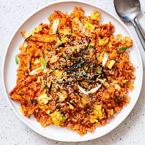 A close-up of Spicy Kimchi Fried Rice with gochujang, crisp carrots, and green onions on a white plate.  