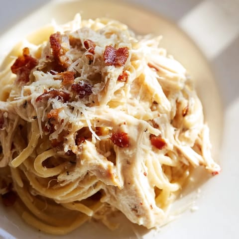 The classic Italian-inspired Chicken Carbonara pasta dish, featuring a heap of spaghetti topped with savory shredded chicken and crispy bacon, ready to serve.  