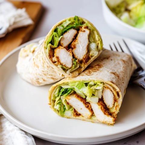Sliced chicken and crisp vegetables wrapped in a tortilla with a drizzle of honey-mustard sauce on a rustic wooden board.  