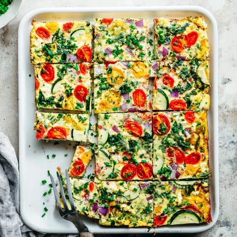 Golden-brown, fluffy sheet pan eggs with cottage cheese and colorful roasted vegetables, sliced into squares and garnished with fresh chives for a high-protein breakfast.