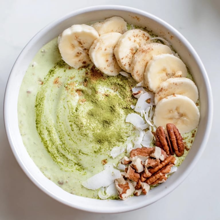 A bowl of vibrant green High-Protein Eggnog Matcha Overnight Oats, boasting hints of cinnamon and nutmeg.