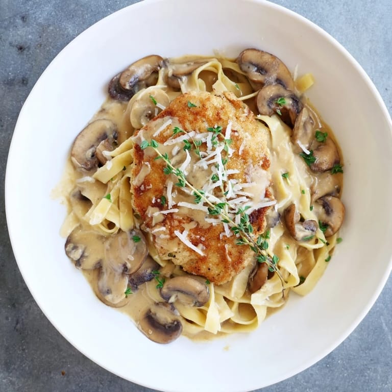 Creamy Chicken Marsala with tender chicken and savory mushrooms in a luscious wine sauce, served alongside a steaming plate of fettuccine.