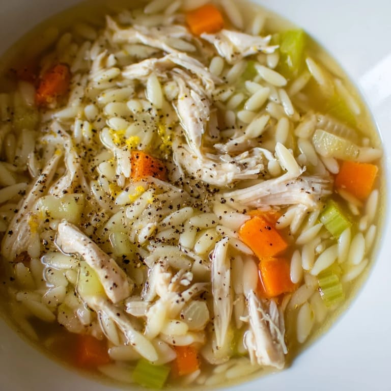 Comforting Lemon Pepper Chicken Orzo Soup ladled from a Dutch oven, featuring orzo pasta and finely sliced carrots in broth.