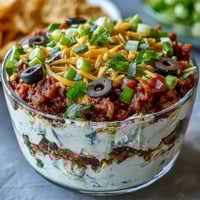 Freshly made 4-Way Layered Dip with vibrant beans, creamy cheese, and fresh salsa, served with tortilla chips.