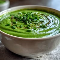 Creamy spinach and white bean soup with vibrant green vegetables in a rustic bowl, garnished with fresh chives.  