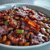 A skillet of baked beans with crispy bacon and brown sugar, bubbling and ready for summer BBQs.